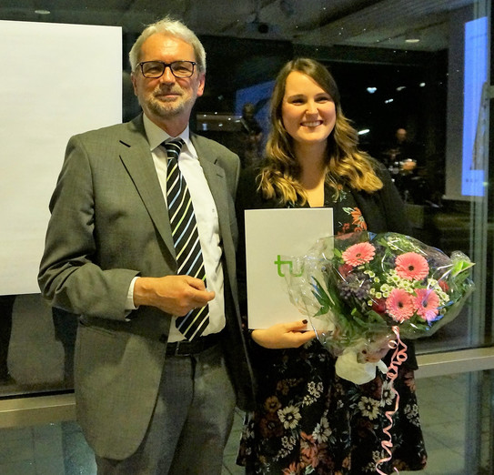 Bild von Dr. Heinrich Tröster und Teresa Mann. Mann in grauem Anzug mit kurzen weißen Haaren und einem kurzen weißem Bart und Brille ist links im Bild und lächelt. Daneben ist eine lächelnde Frau mit einem schwarzen Kleid mit rosa Blumen. Sie hat lange braune gewellte Haare und hält einen Blumenstrauß in einer und ein Dokument in der anderen Hand.