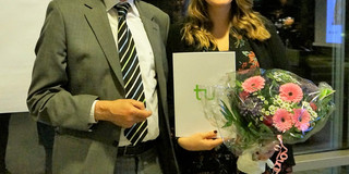 Lotte Kaliski Preis 2018 Bild von Dr. Heinrich Tröster und Teresa Mann. Mann in grauem Anzug mit kurzen weißen Haaren und einem kurzen weißem Bart und Brille ist links im Bild und lächelt. Daneben ist eine lächelnde Frau mit einem schwarzen Kleid mit rosa Blumen. Sie hat lange braune gewellte Haare und hält einen Blumenstrauß in einer und ein Dokument in der anderen Hand.