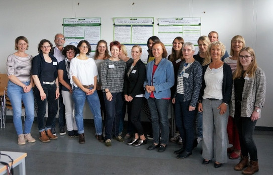 Gruppenfoto mit 18 Personen vor drei Plakaten